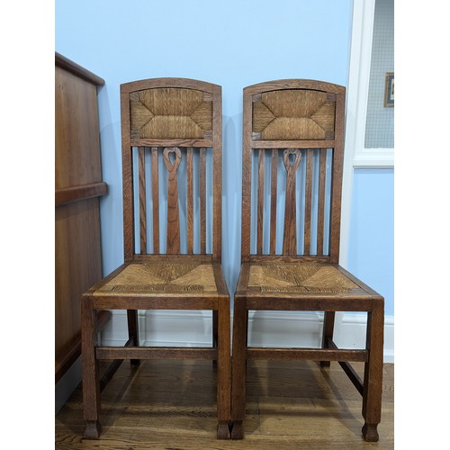 415 - In the manner of Liberty a pair of Arts and Crafts oak Hall Chairs, rush headrests over spindle back... 