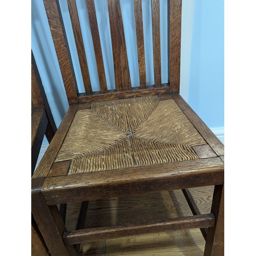 415 - In the manner of Liberty a pair of Arts and Crafts oak Hall Chairs, rush headrests over spindle back... 