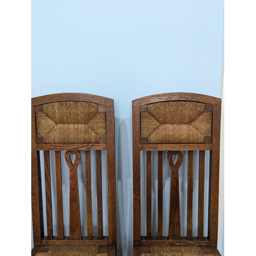 415 - In the manner of Liberty a pair of Arts and Crafts oak Hall Chairs, rush headrests over spindle back... 