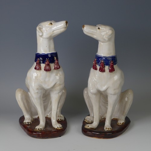 37 - A pair of mid 20thC majolica pottery Greyhounds, modelled in a seated position with tail resting on ... 