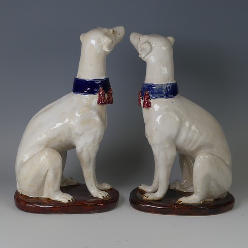 37 - A pair of mid 20thC majolica pottery Greyhounds, modelled in a seated position with tail resting on ... 