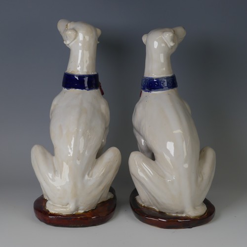 37 - A pair of mid 20thC majolica pottery Greyhounds, modelled in a seated position with tail resting on ... 