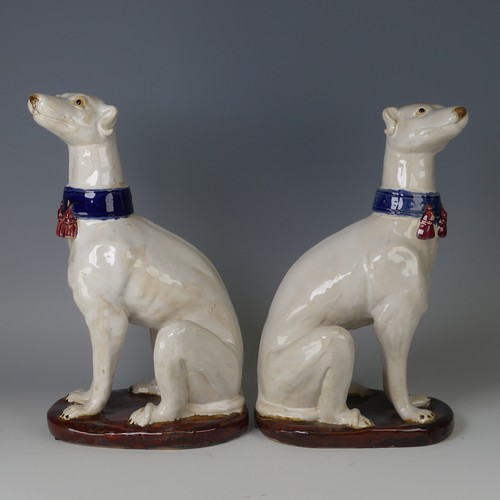 37 - A pair of mid 20thC majolica pottery Greyhounds, modelled in a seated position with tail resting on ... 