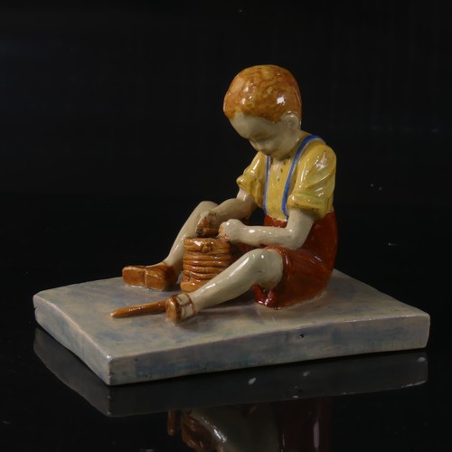 54 - Isobel Holland (1913-1986) a Clevedon Pottery figure of a Boy, modelled sat upright potting with a t... 