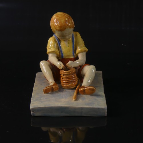 54 - Isobel Holland (1913-1986) a Clevedon Pottery figure of a Boy, modelled sat upright potting with a t... 