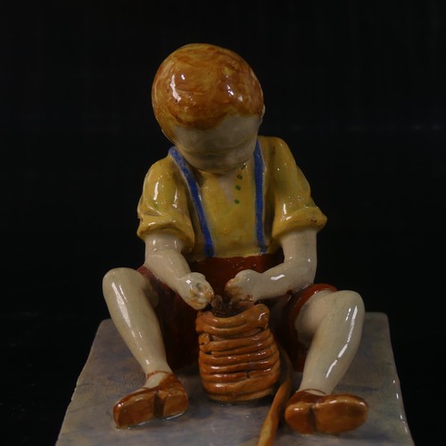 54 - Isobel Holland (1913-1986) a Clevedon Pottery figure of a Boy, modelled sat upright potting with a t... 