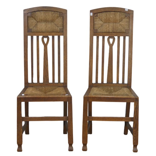 523 - In the manner of Liberty a pair of Arts and Crafts oak Hall Chairs, rush headrests over spindle back... 