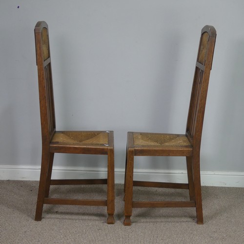 523 - In the manner of Liberty a pair of Arts and Crafts oak Hall Chairs, rush headrests over spindle back... 