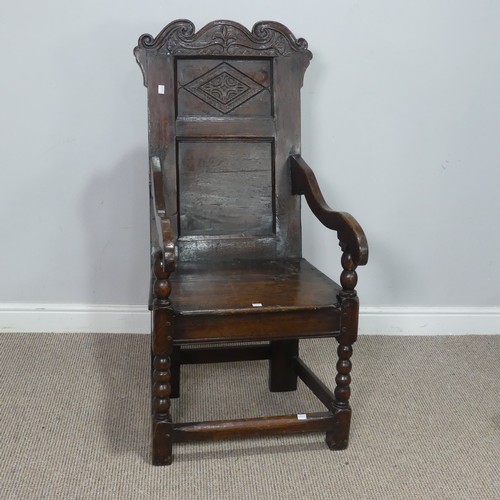 A 17th century oak wainscot Chair, the shaped headrest with carved details, over square seat flanked by scrolled armrests, W 51 cm x H 113 cm x D 60 cm.