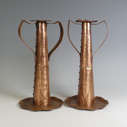 A pair of Arts and Crafts copper Candlesticks, probably by Eustace Brothers, each having a pair of shaped handles, planished decoration with shield shaped detail, and with shaped circular bases embossed with fish, H 30.5 cm(2)