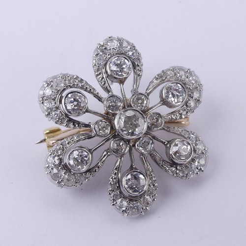 A diamond cluster foliate Pendant / Brooch, the central stone c. 0.25ct, with six smaller stones around each, those with larger stones on knifewires between, all collet set within a six petalled surround set with gradated diamonds, correspondingly set suspension loop, all mounted in unmarked white metal, tested as platinum, the reverse with screw fitting brooch pin, marked '750', 2.8cm diameter, 11g.