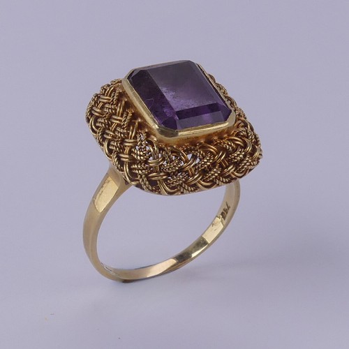 134 - An amethyst Dress Ring, the emerald cut stone approx. 11.6mm x 9.2mm, collet set within an elaborate... 