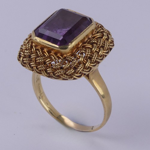 134 - An amethyst Dress Ring, the emerald cut stone approx. 11.6mm x 9.2mm, collet set within an elaborate... 