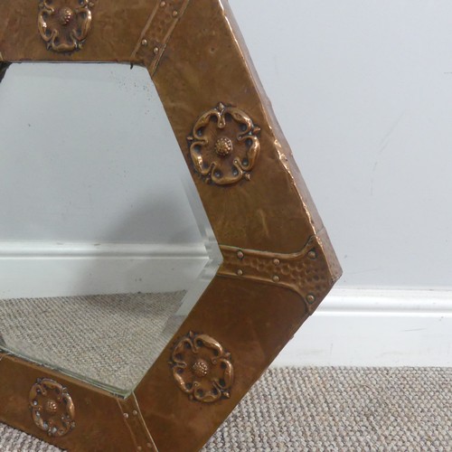 519 - An Arts and Crafts copper hexagonal Mirror, the hammered frame embossed with flower motifs encasing ... 