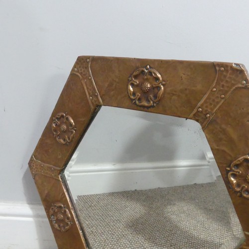 519 - An Arts and Crafts copper hexagonal Mirror, the hammered frame embossed with flower motifs encasing ... 