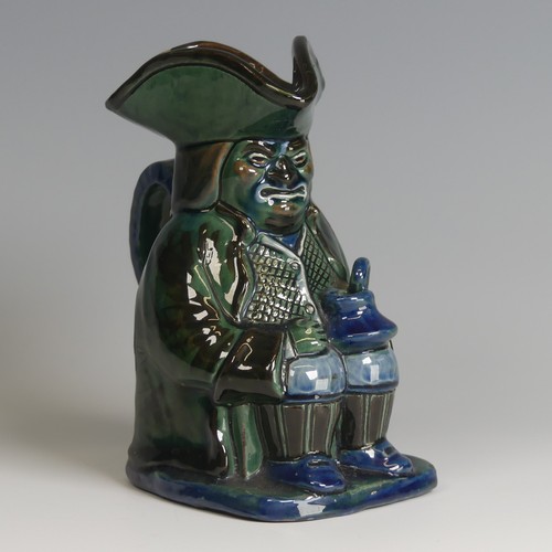 63 - A C. H. Brannam pottery Character Jug, decorated as a seated man with jug in hand in tones of blue, ... 