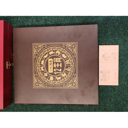 322 - A BOXED BOOKLET CONTAINING 12 GOLD PLATED CHINESE COINS DEPICTING THE CHINESE YEARS - IN WOODEN FOLD... 