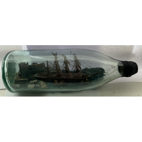 371 - A VINTAGE SHIP IN BOTTLE DIORAMA SHOWING A FOUR MASTED SHIP WITH TWO SMALLER VESSELS LEAVING A PORT ... 