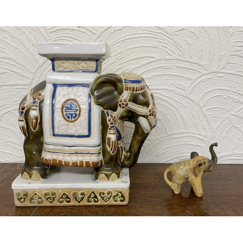 402 - X2 ELEPHANT FIGURINES - ONE CARVED WOODEN ELEPHANT AND ONE ORNATE CERAMIC BLUE, WHITE AND RED STANDI... 