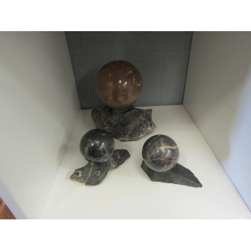 1249 - Three polished stone balls on rock stands, largest 11cm diameter