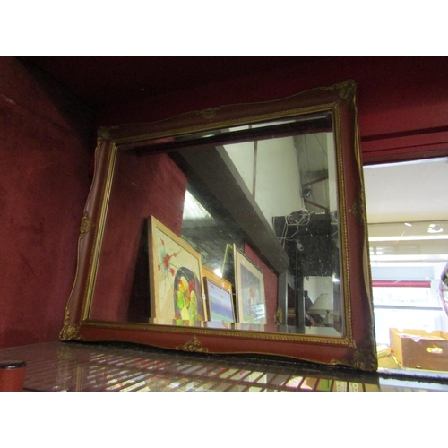 4377 - A red and gilt ornately framed wall mirror with bevel edge, 53.5cm high x 63.5cm wide     (C)