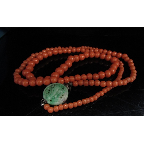 6184 - A graduated coral bead necklace with a carved jade clasp, stamped silver, 68cm long