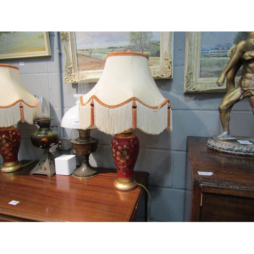 1057 - A pair of red and gilt floral design table lamps with tasselled shades