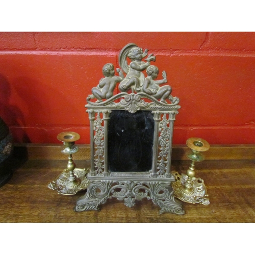 4147 - An elaorate heavy metal mirror adorned with cherubs and a pair of ornate brass candlesticks