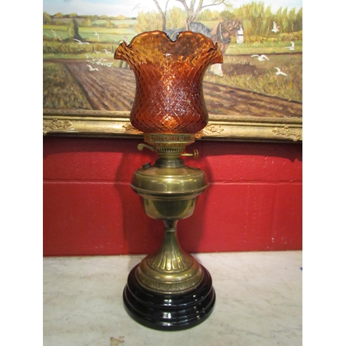 4160 - A brass based oil lamp with a pink/red scalloped floral form shade, black porcelain base