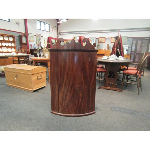 1052 - A Georgian mahogany bow fronted wall-hanging corner cabinet, scrolled crest over single door opening... 