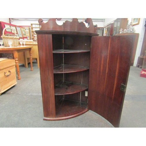 1052 - A Georgian mahogany bow fronted wall-hanging corner cabinet, scrolled crest over single door opening... 