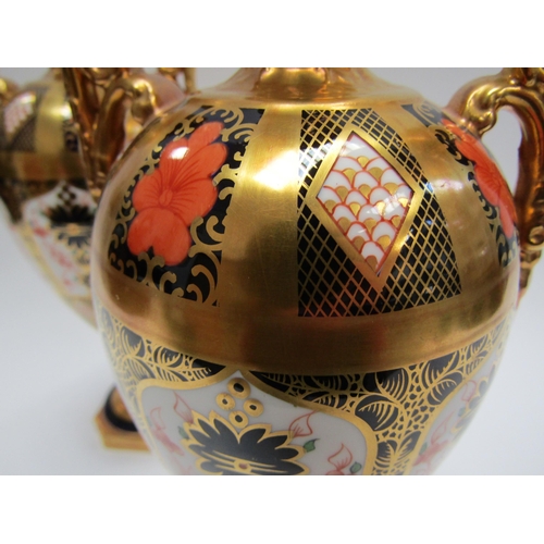 5116 - A pair of Royal Crown Derby Imari pattern urns, ovoid form with fixed knop cover and two high loop h... 