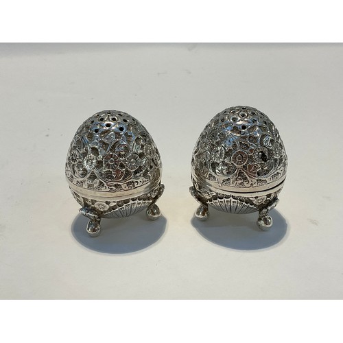 5064 - A pair of white metal egg form salt and pepperette shakers, all over foliate and floral design, cabr... 