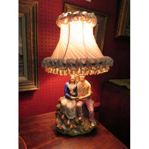 4026 - A Staffordshire table lamp in the form of a courting couple together with a silk pleated and tassell... 