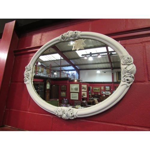 4150 - A painted white oval frame wall mirror with carved rose decoration, 60cm high x 80cm wide