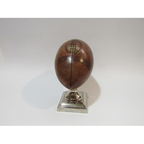 4277 - A walnut rugby ball desk top trophy on a stepped chrome square base, 21cm high