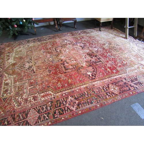 1016 - An Iranian wool Heriz rug.  Red ground and geometric design.  Faded.  330cm x 235cm