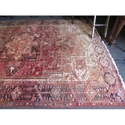 1016 - An Iranian wool Heriz rug.  Red ground and geometric design.  Faded.  330cm x 235cm