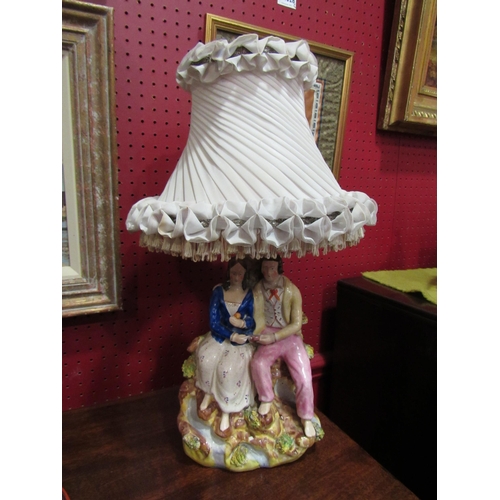 4038 - A Staffordshire table lamp in the form of a courting couple together with a silk pleated and tassell... 