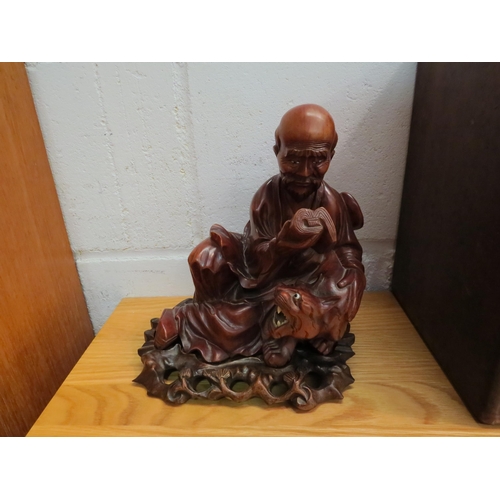 1034 - An Eastern mid-20th Century carved hardwood figure of a sage reading book seated by a tiger on a fit... 