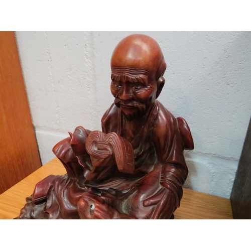 1034 - An Eastern mid-20th Century carved hardwood figure of a sage reading book seated by a tiger on a fit... 