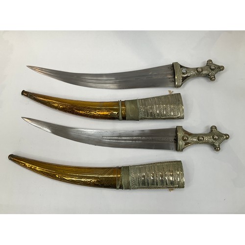 9182 - A near pair of middle eastern decorative short swords, engraved brass and white metal covered scabba... 