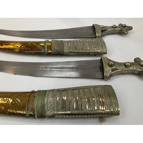 9182 - A near pair of middle eastern decorative short swords, engraved brass and white metal covered scabba... 