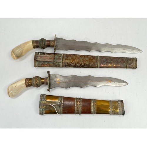 9504 - Two eastern decorative kris-style daggers, both with bone handles, copper and brass hilts and scabba... 