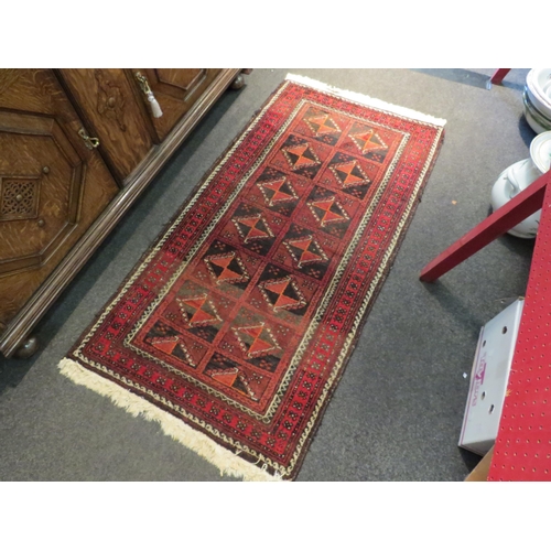 1048 - An Eastern red ground geometric design rug with tasselled ends, 153cm x 82cm