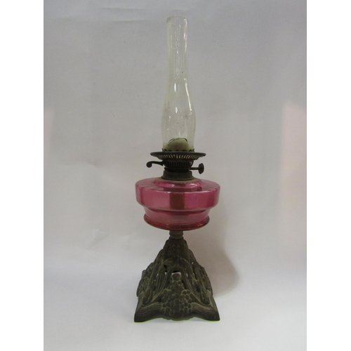 4246 - An oil lamp with cranberry glass reservoir on cast iron base and having a Duplex burner and oval bul... 