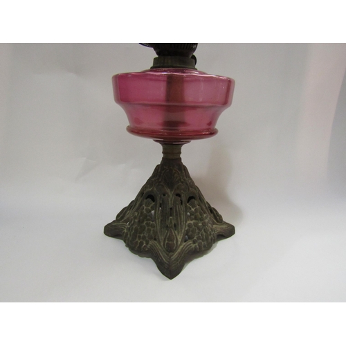 4246 - An oil lamp with cranberry glass reservoir on cast iron base and having a Duplex burner and oval bul... 