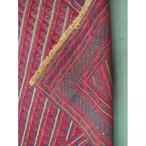 4004 - A square red and blue ground wool rug, striped central panel with multiple borders to tasselled ends... 