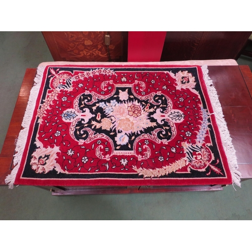 4123 - A small red ground hand woven wool bedside/table rug with central foliate panel and tasselled ends, ... 