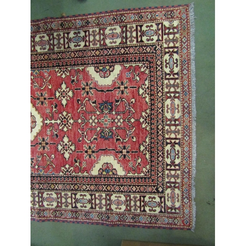 4023 - A red ground wool rug with multiple borders, 182cm x 113cm